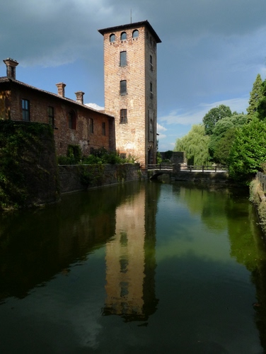 Immagine con torre, finestre, alberi, acqua, riflesso, verde, comignoli, fiume, nuvole, cielo, ponte, casa, camini, case, canale, edificio