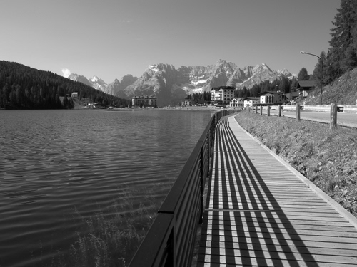 Immagine con lago, bianconero, acqua, montagne, ringhiera, strada, passeggiata, ombre, ombra, alberi, prospettiva, montagna, staccionata, case