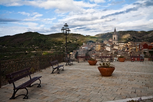 Immagine con panchine, campanile, vasi, piazza, lampione, case, paese, cielo, colline, nuvole, piante, terrazza, scorcio, borgo, paesaggio, montagne, chiesa, belvedere, panorama, ringhiera